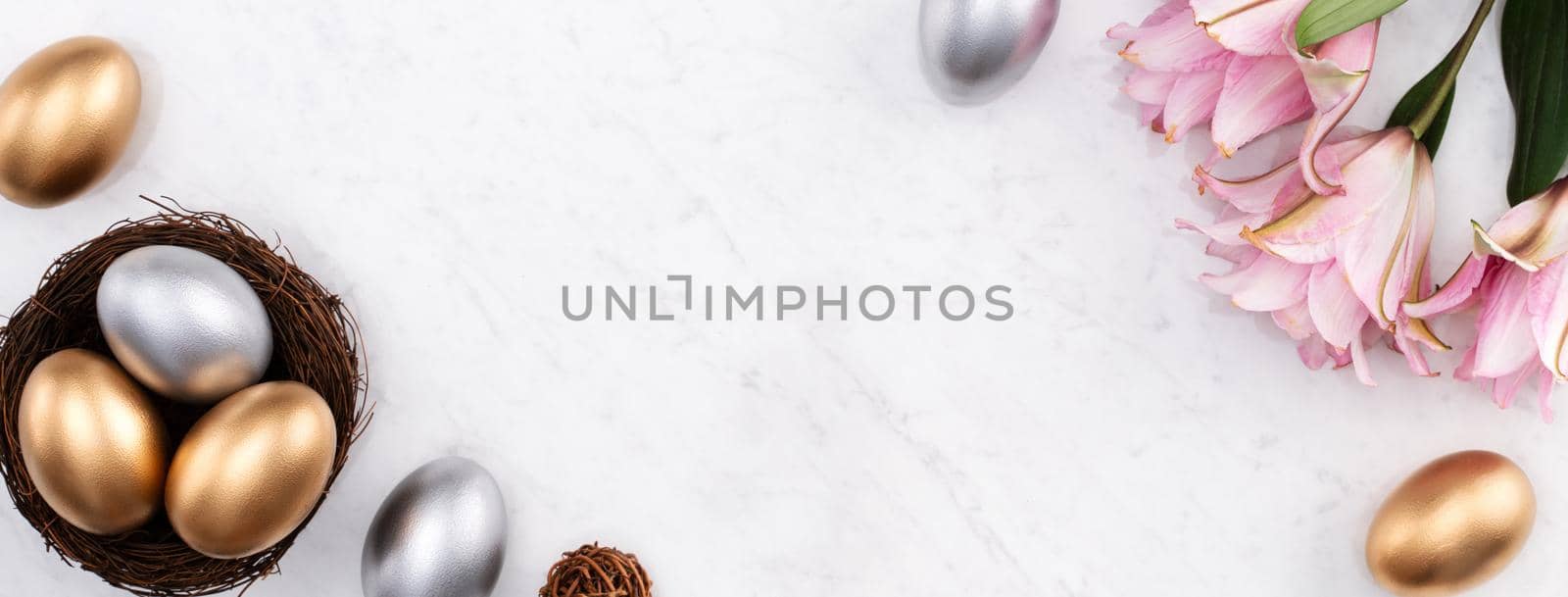 Design concept of Golden and silver Easter eggs in the nest with pink lily flower on bright marble white table background.