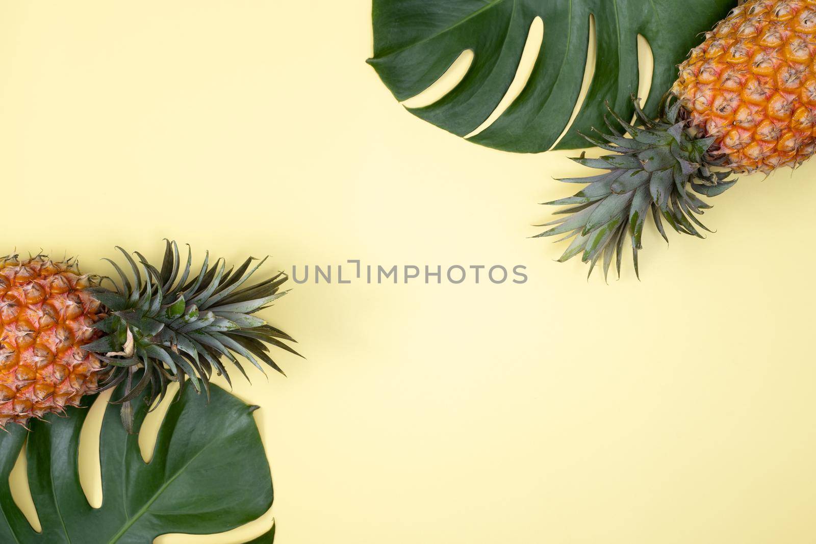 Top view of fresh pineapple with tropical leaves on yellow background. by ROMIXIMAGE