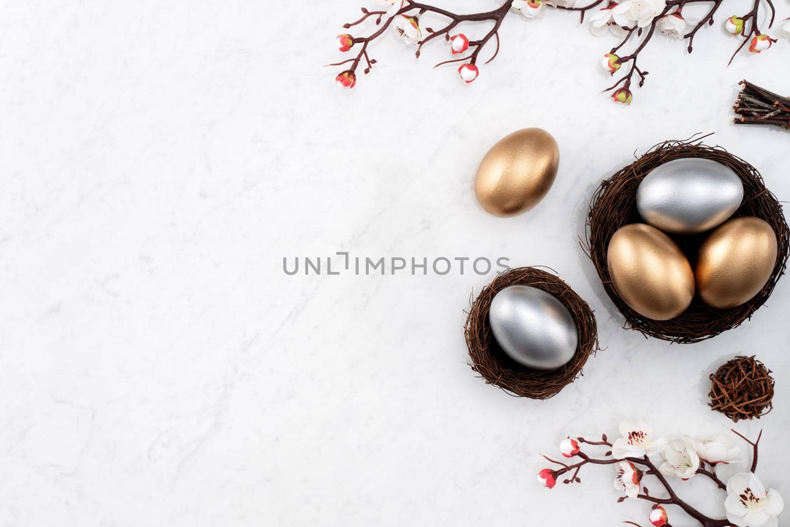 Design concept of Golden and silver Easter eggs in the nest with white plum flower on bright marble white table background.
