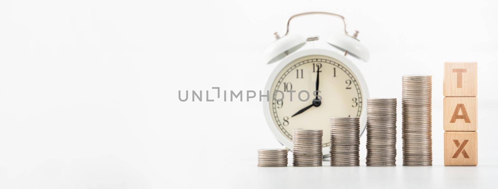 Concept of tax season approaching with wooden blocks, coins and alarm clock over white background.