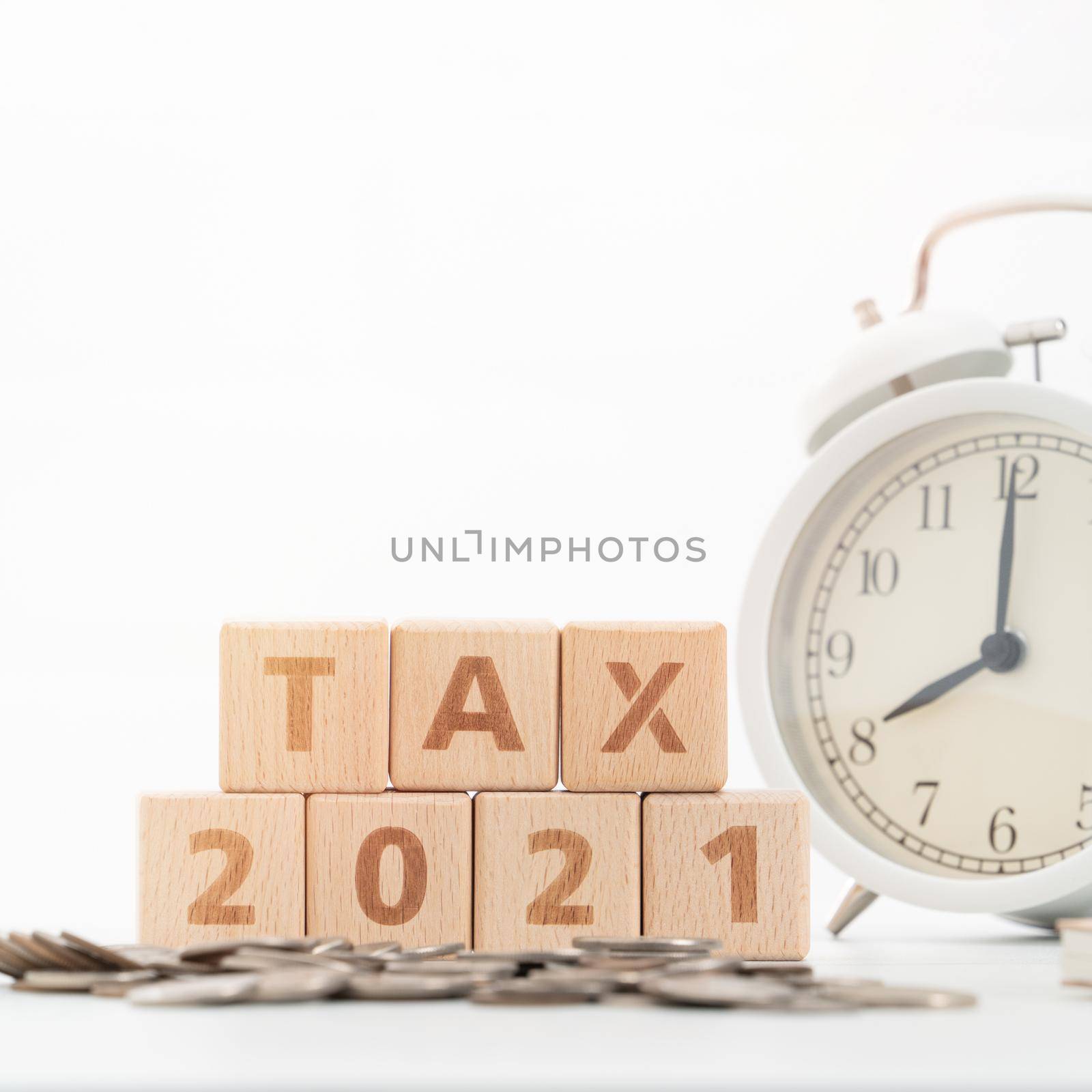 Concept of tax season approaching with wooden blocks, coins and alarm clock over white background.