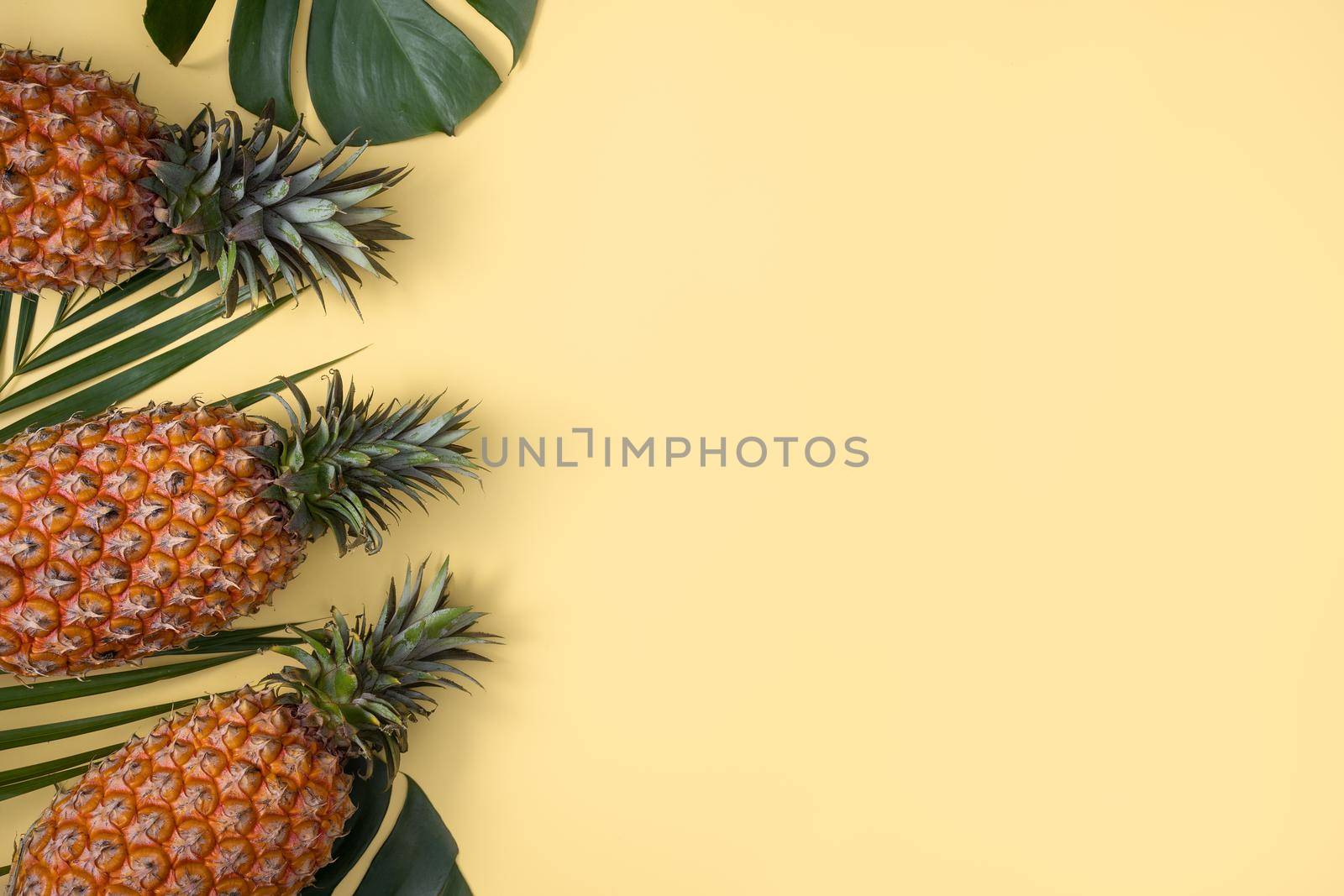 Top view of fresh pineapple with tropical leaves on yellow background. by ROMIXIMAGE