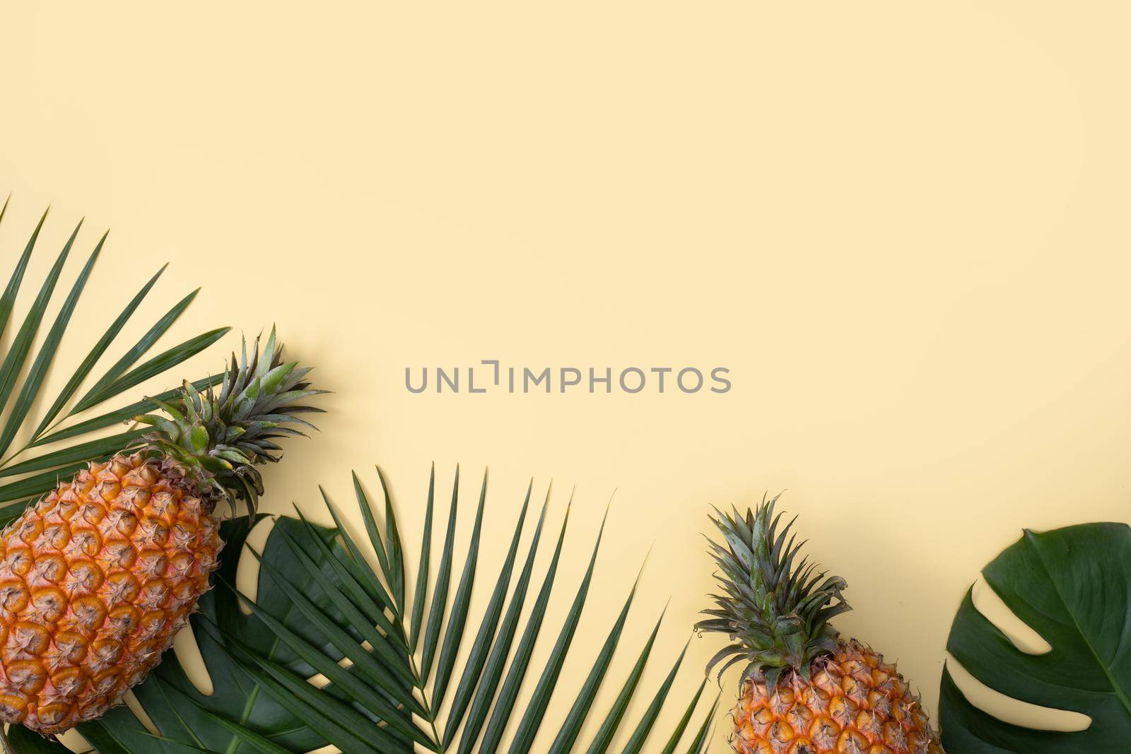 Top view of fresh pineapple with tropical palm and monstera leaves on yellow table background.