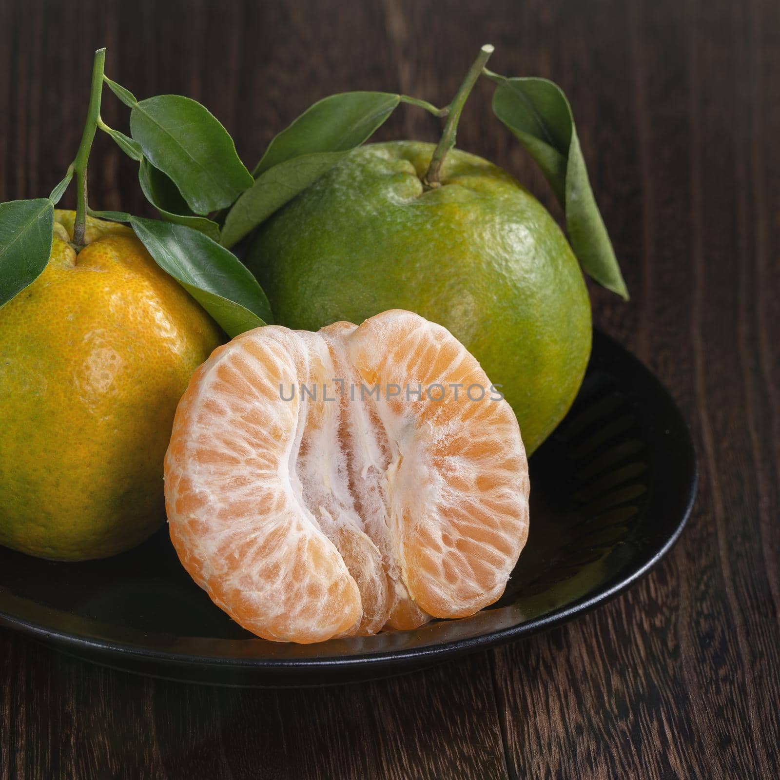 Fresh green tangerine mandarin orange with fresh leaves on dark wooden table background harvest concept.