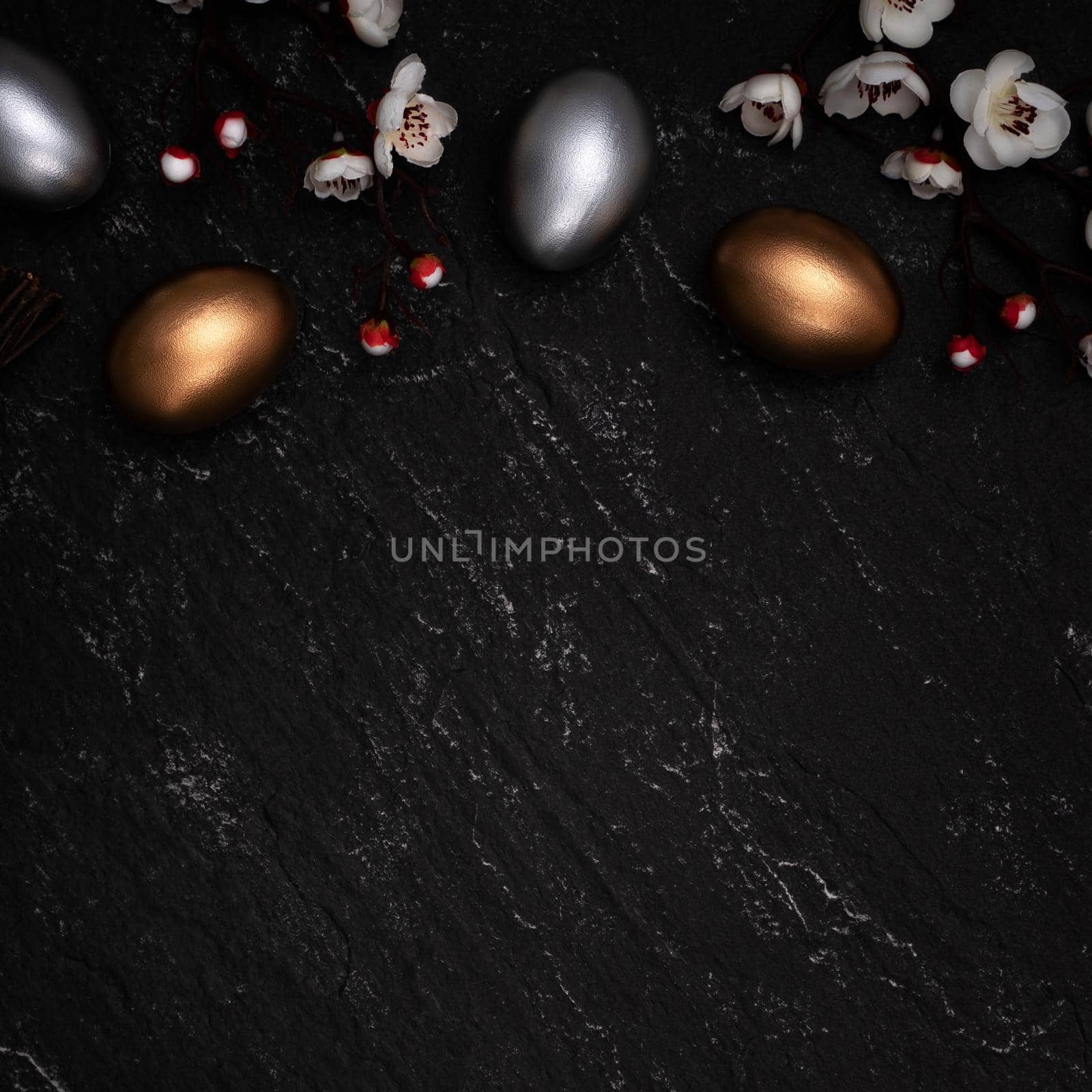 Golden and silver Easter eggs with plum blossom flower on dark black slate table background.