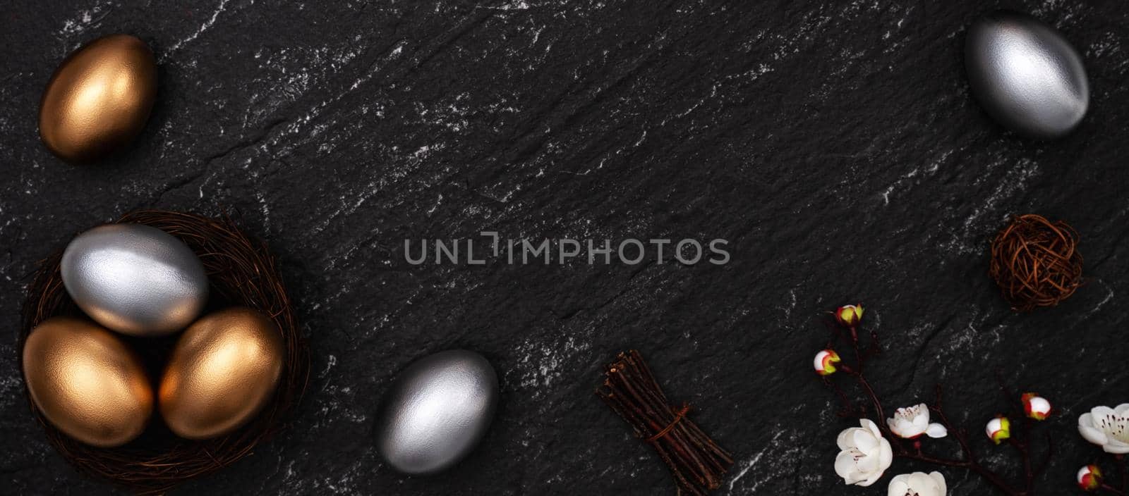 Golden and silver Easter eggs with plum blossom flower on dark black slate table background.