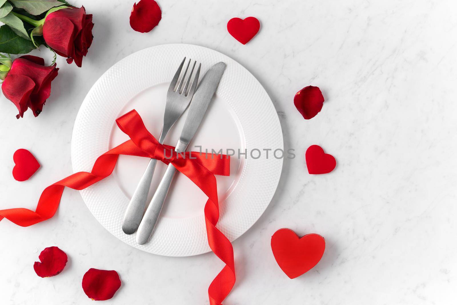 White plate with red rose flower on marble white table background for Valentine's Day dating holiday meal concept.