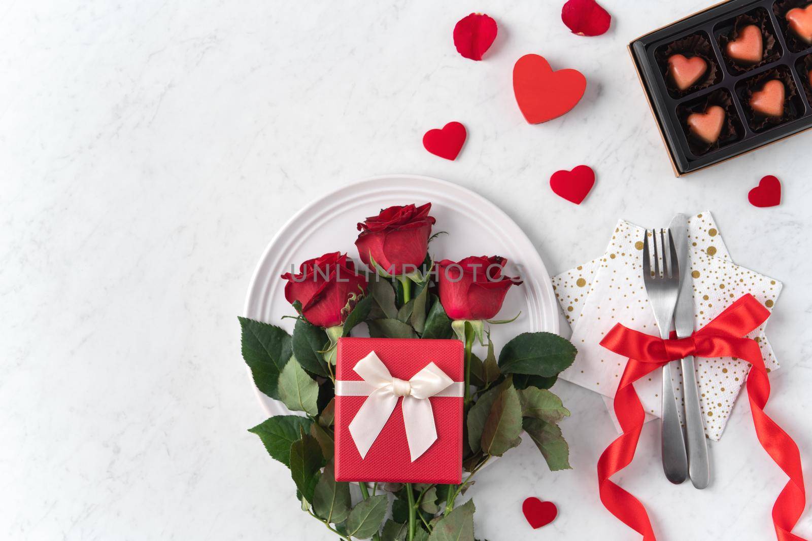 White plate with red rose flower on marble white table background for Valentine's Day dating holiday meal concept.