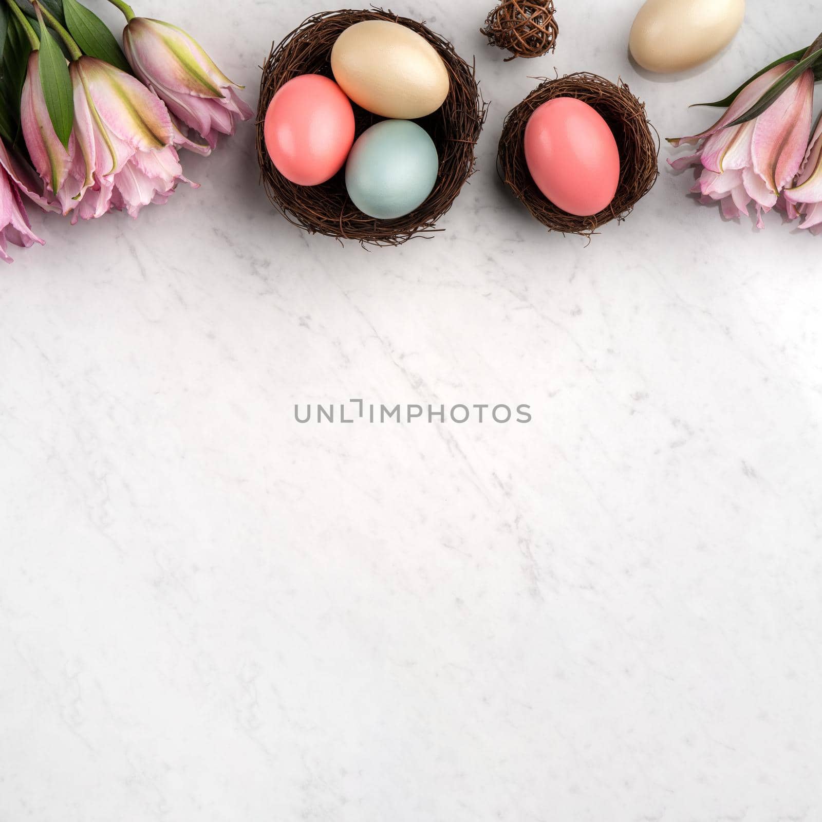 Colorful Easter eggs in the nest with pink lily flower on bright marble white table background.