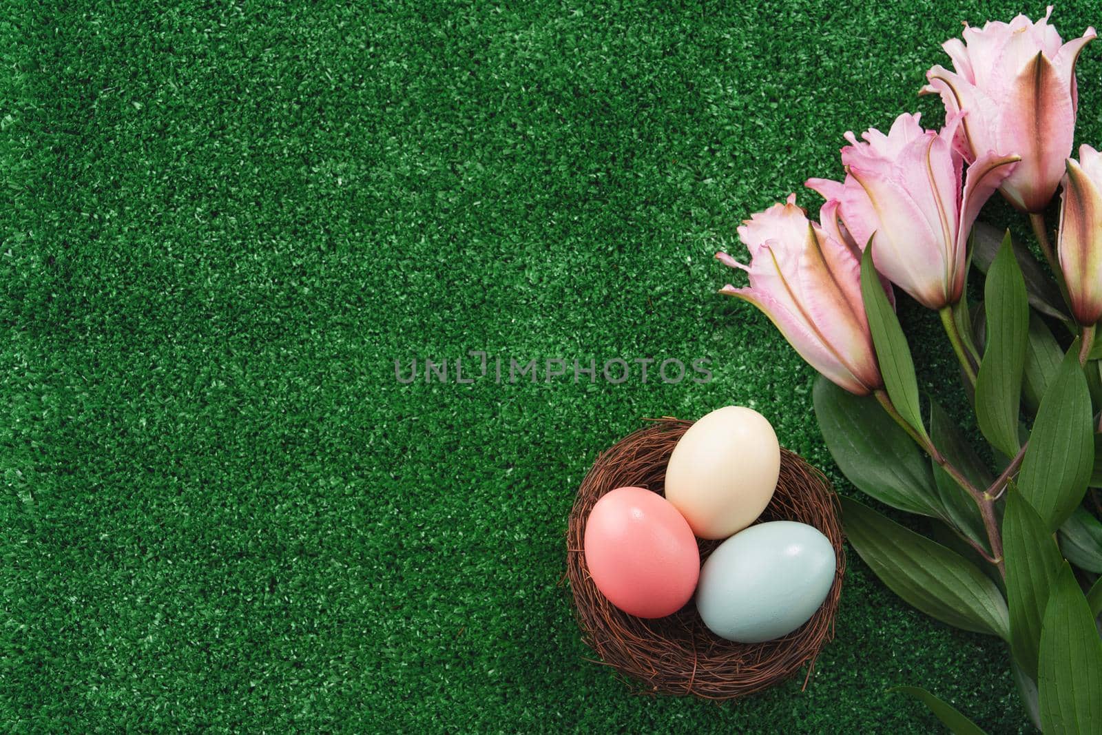 Colorful Easter eggs in the nest with pink lily flower on on a lawn grass background.