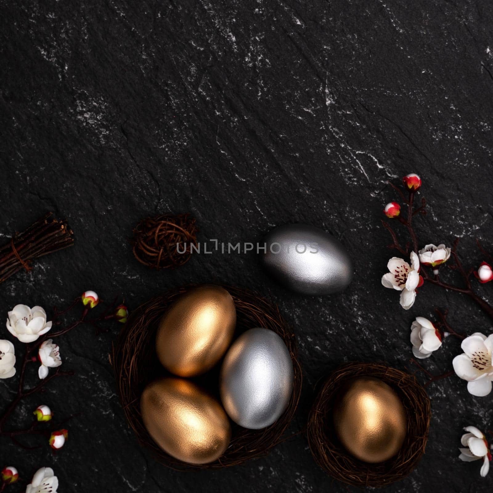 Golden and silver Easter eggs with plum blossom flower on dark black slate table background.