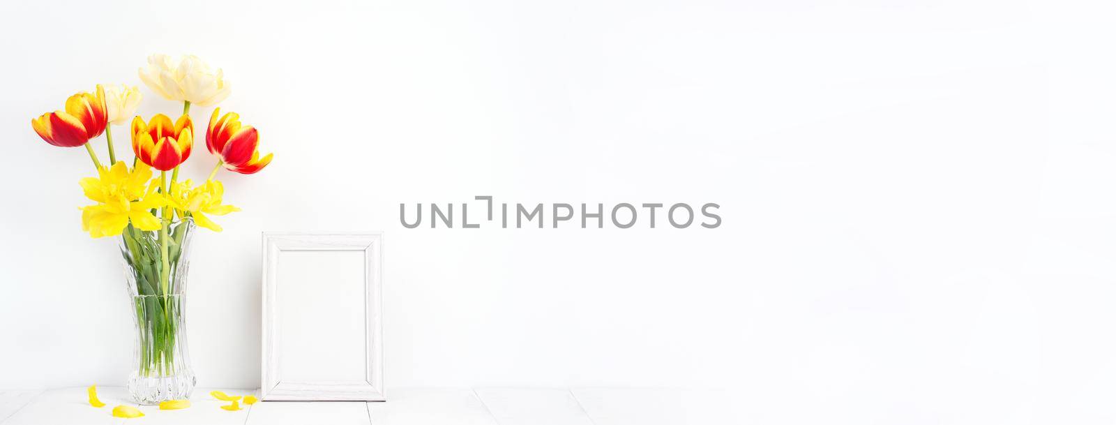 Tulip flower in glass vase with picture frame on white wall, Mother's Day decor concept.