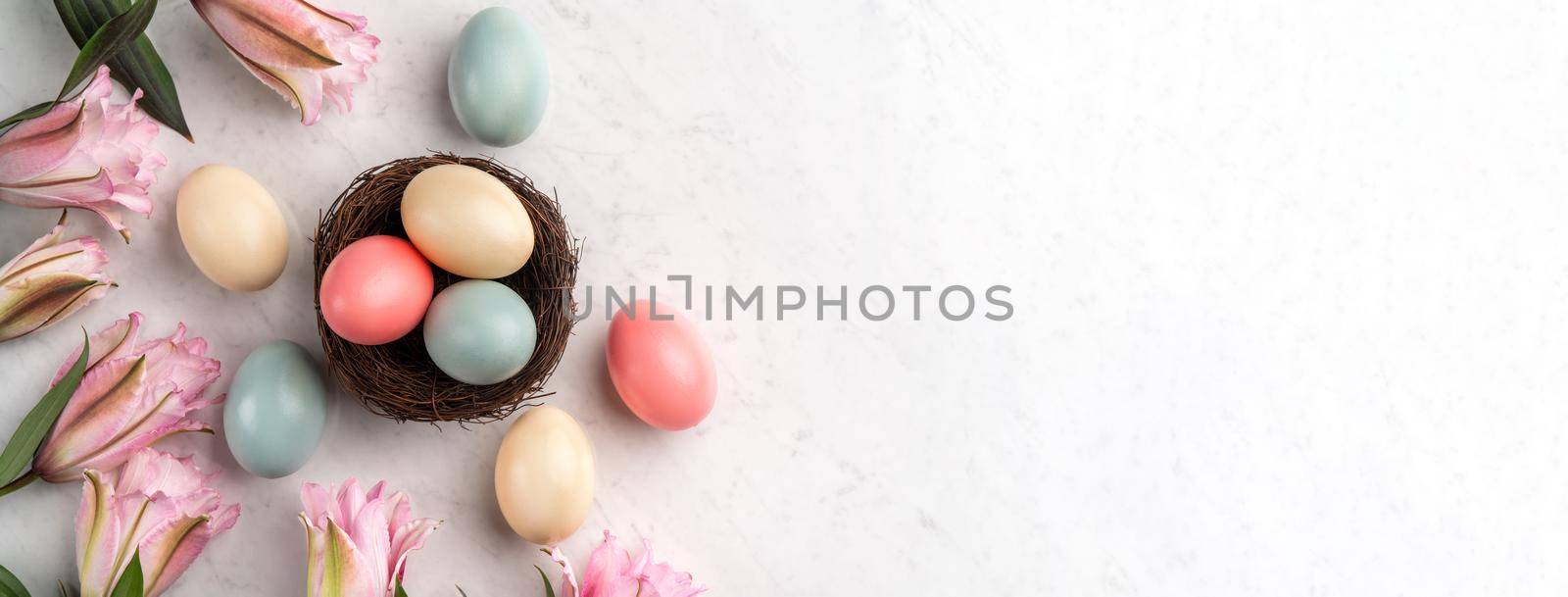 Colorful Easter eggs in the nest with pink lily flower on bright marble white table background.