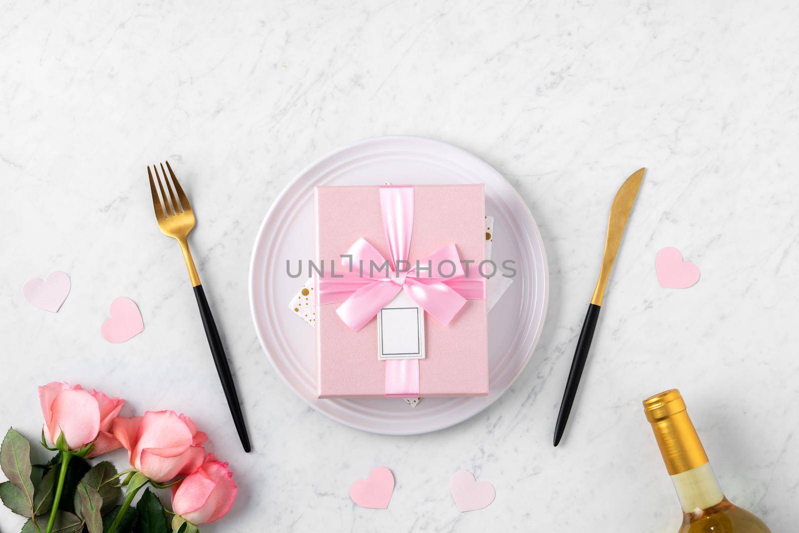 White plate with gift and pink rose flower on marble white table background for Valentine's Day special holiday dating meal concept.