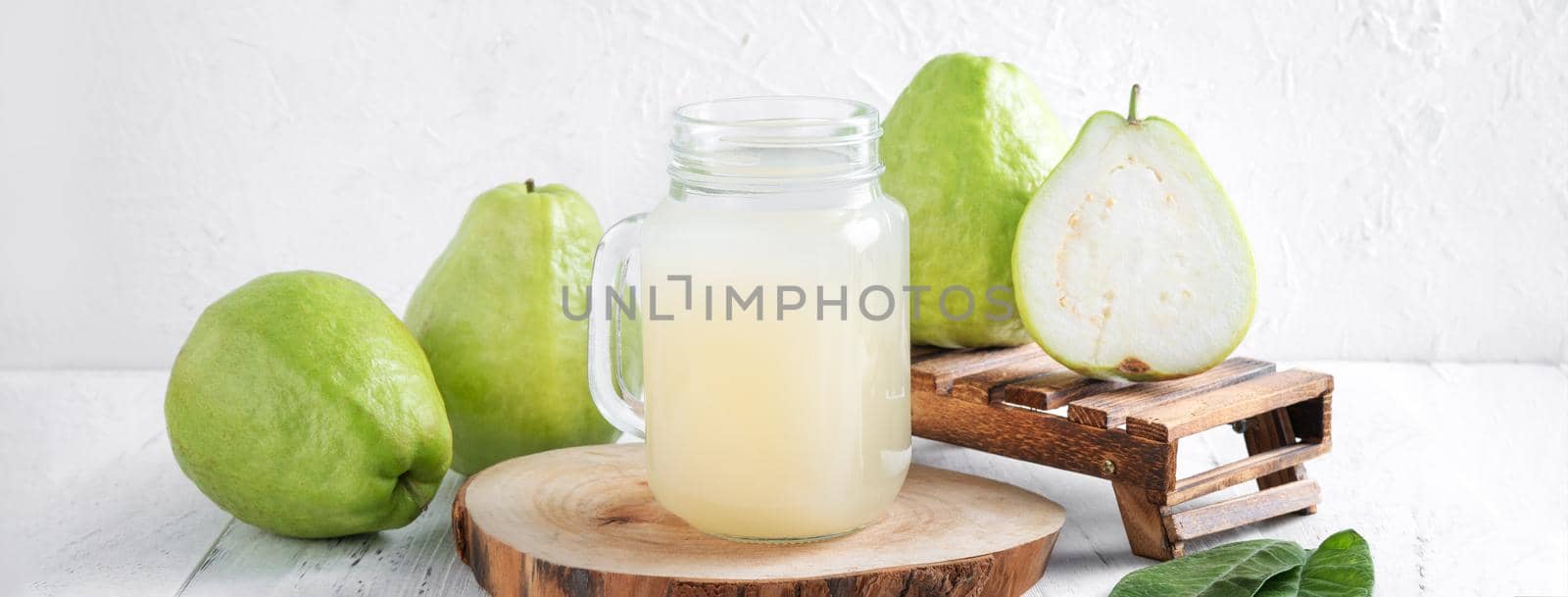 Delicious beautiful guava fruit with fresh juice set isolated on bright white wooden table background, close up.