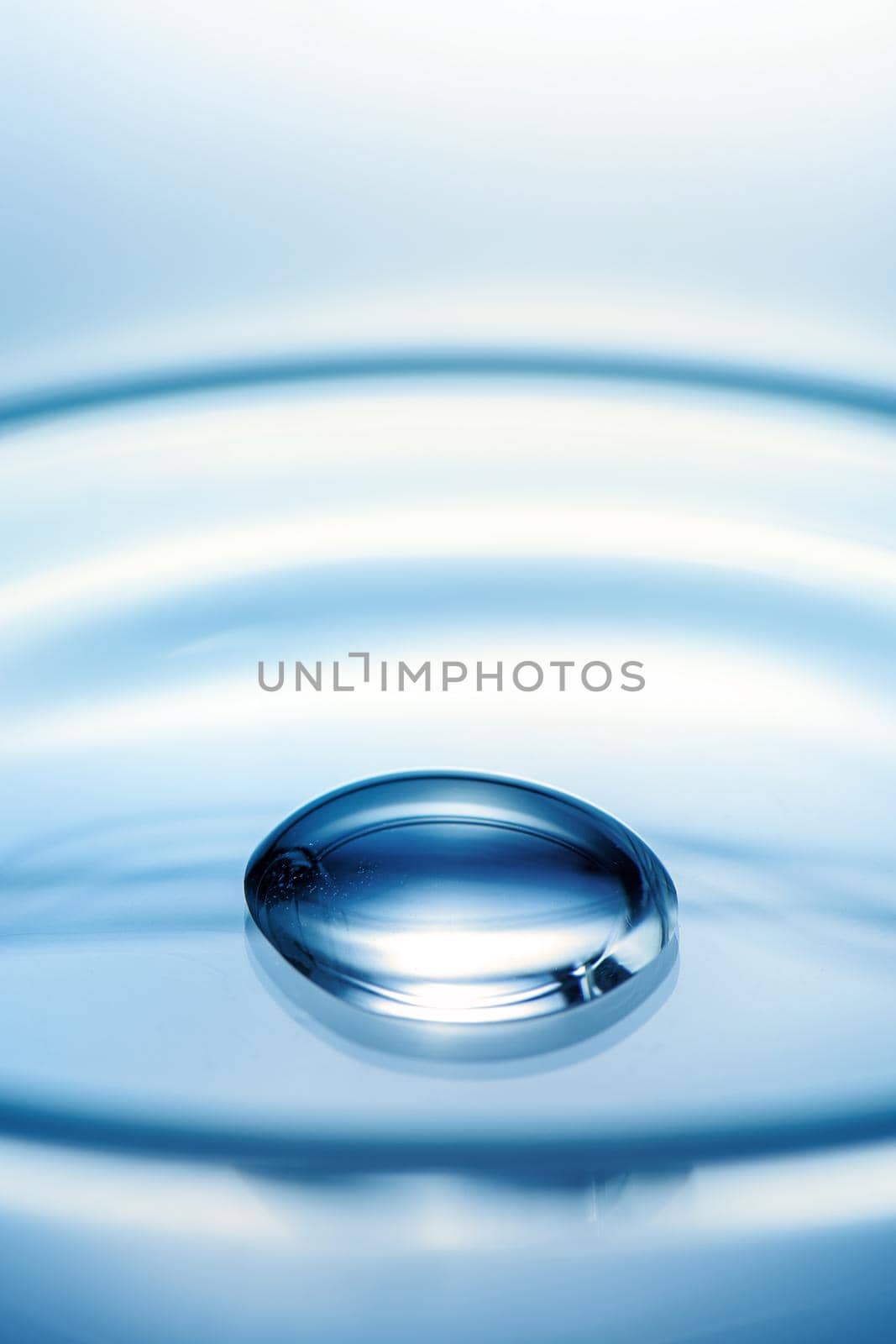Clean glass petri dish with liquid drop inside over blue light background, concept of science lab test and vaccine development.