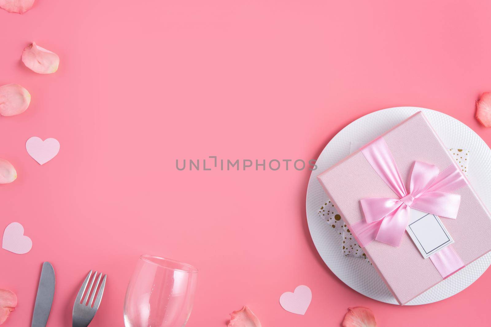 Empty white plate with gift and rose petals for Valentine's Day special holiday dating meal concept.