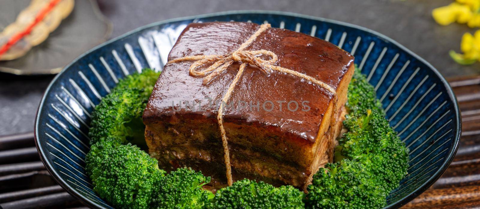 Dong Po Rou (Dongpo pork meat) in a beautiful blue plate with green broccoli vegetable, traditional festive food for Chinese new year cuisine meal, close up.