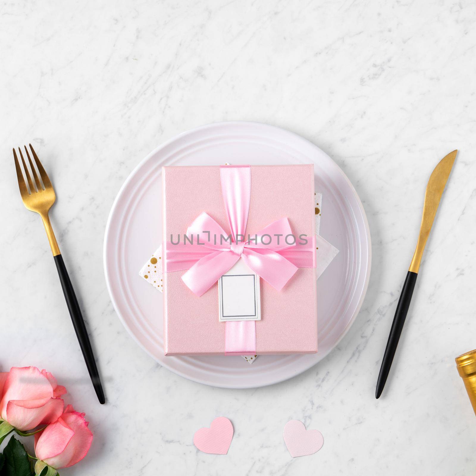 White plate with gift and pink rose flower on marble white table background for Valentine's Day special holiday dating meal concept.