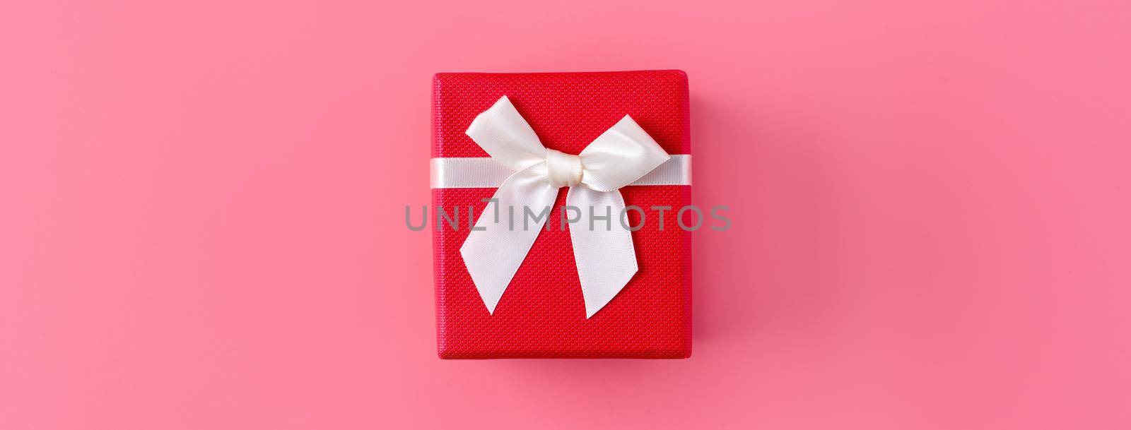 Beautiful gift box wrapped with ribbon bow on pastel pink background.
