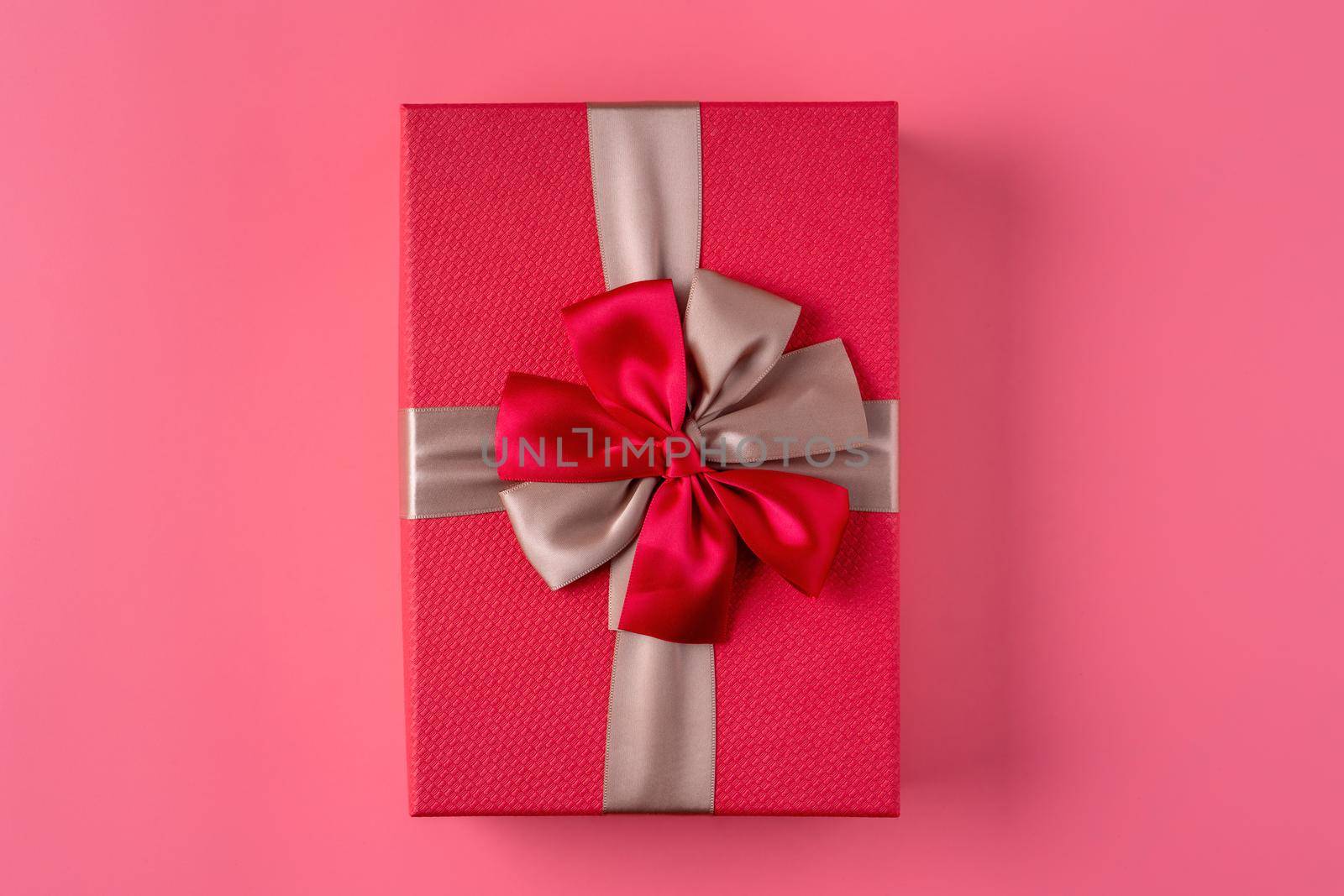 Beautiful gift box wrapped with ribbon bow on pastel pink background.