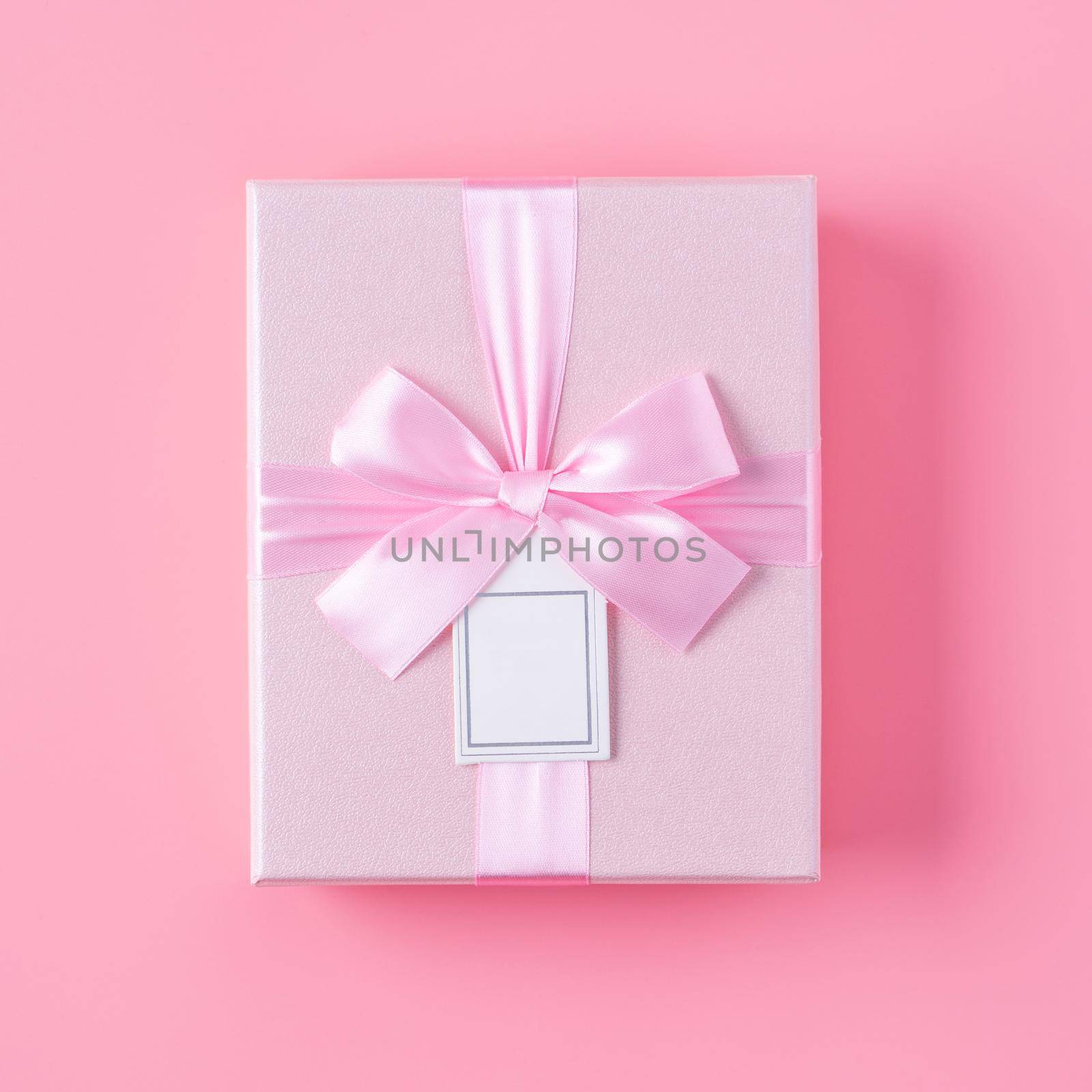 Beautiful gift box wrapped with ribbon bow on pastel pink background.