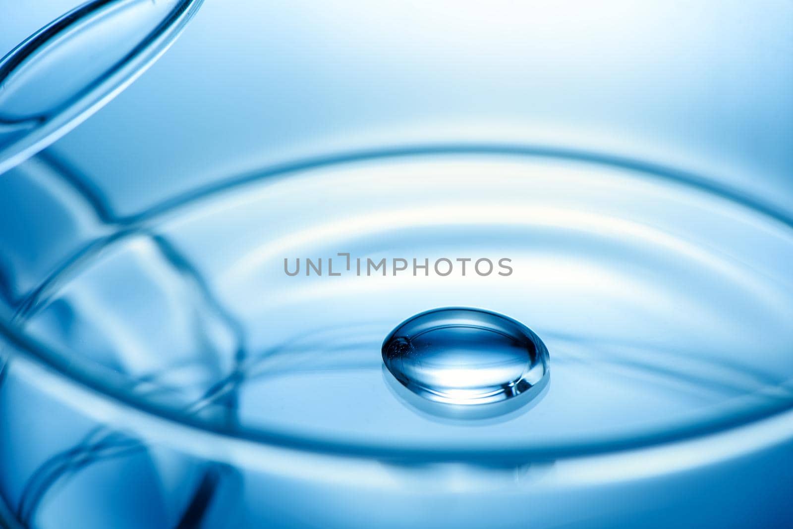 Clean glass petri dish with liquid drop inside over blue light background, concept of science lab test and vaccine development.