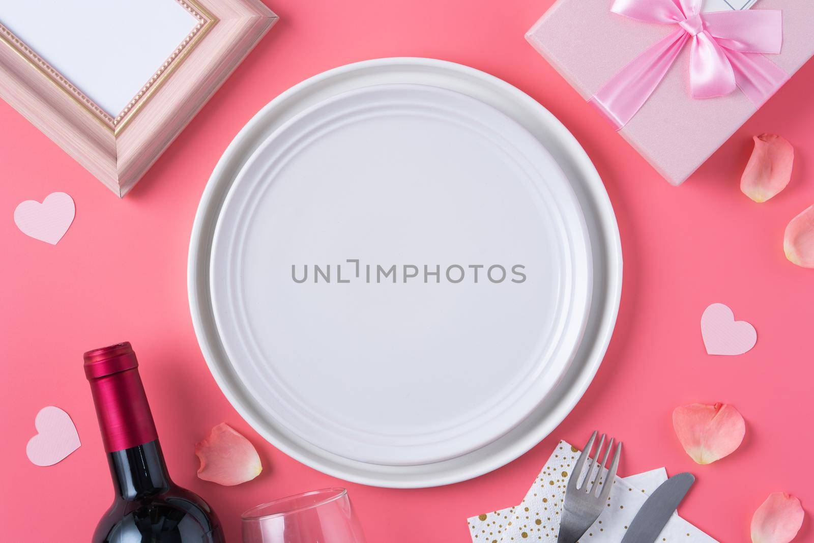 Empty white plate with gift and rose petals for Valentine's Day special holiday dating meal concept.