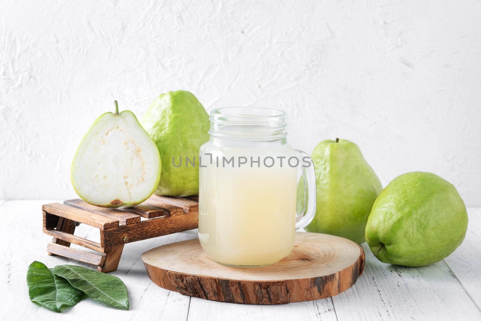 Delicious beautiful guava fruit with fresh juice set isolated on bright white wooden table background, close up.