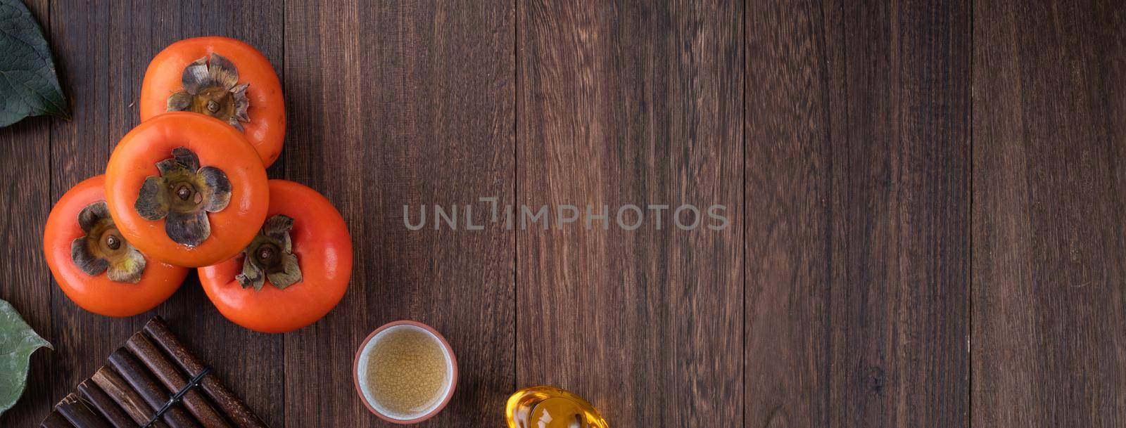 Top view of fresh sweet persimmons kaki with leaves on wooden table background for Chinese lunar new year fruit design concept, the word means blessing is coming.