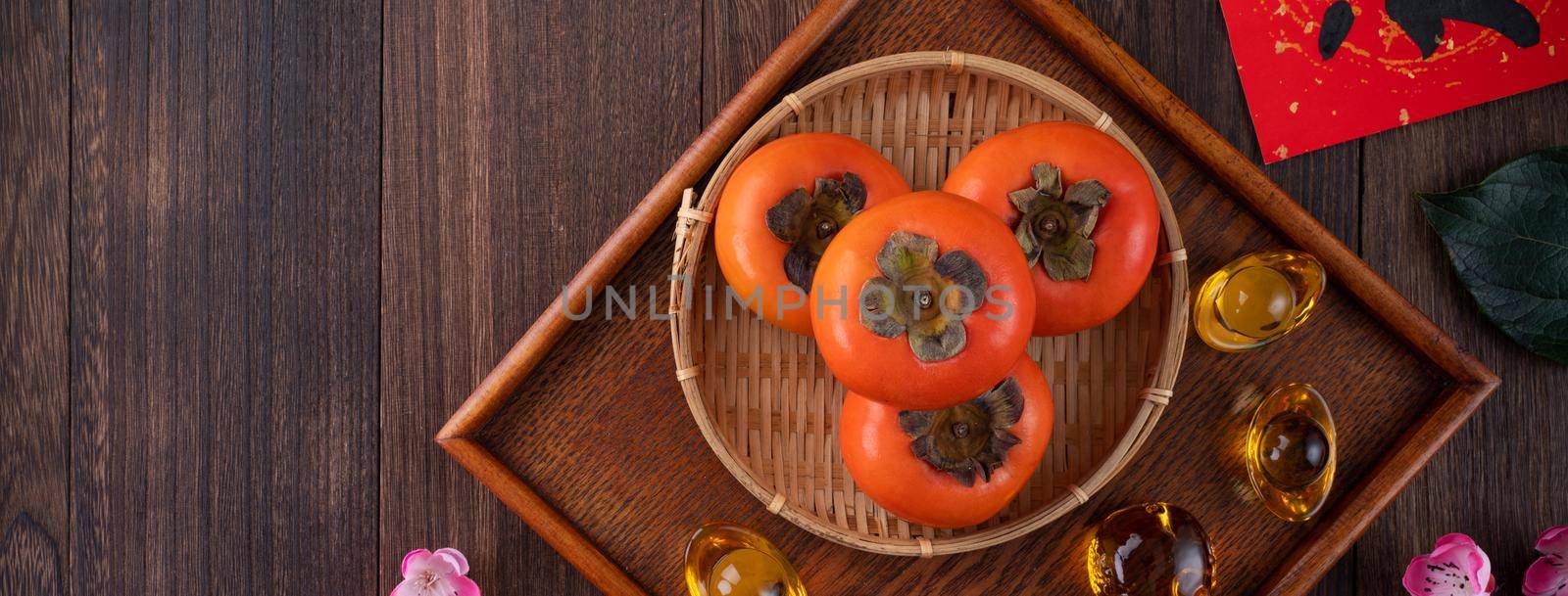 Top view of fresh sweet persimmons kaki with leaves on wooden table background for Chinese lunar new year fruit design concept, the word means blessing is coming.