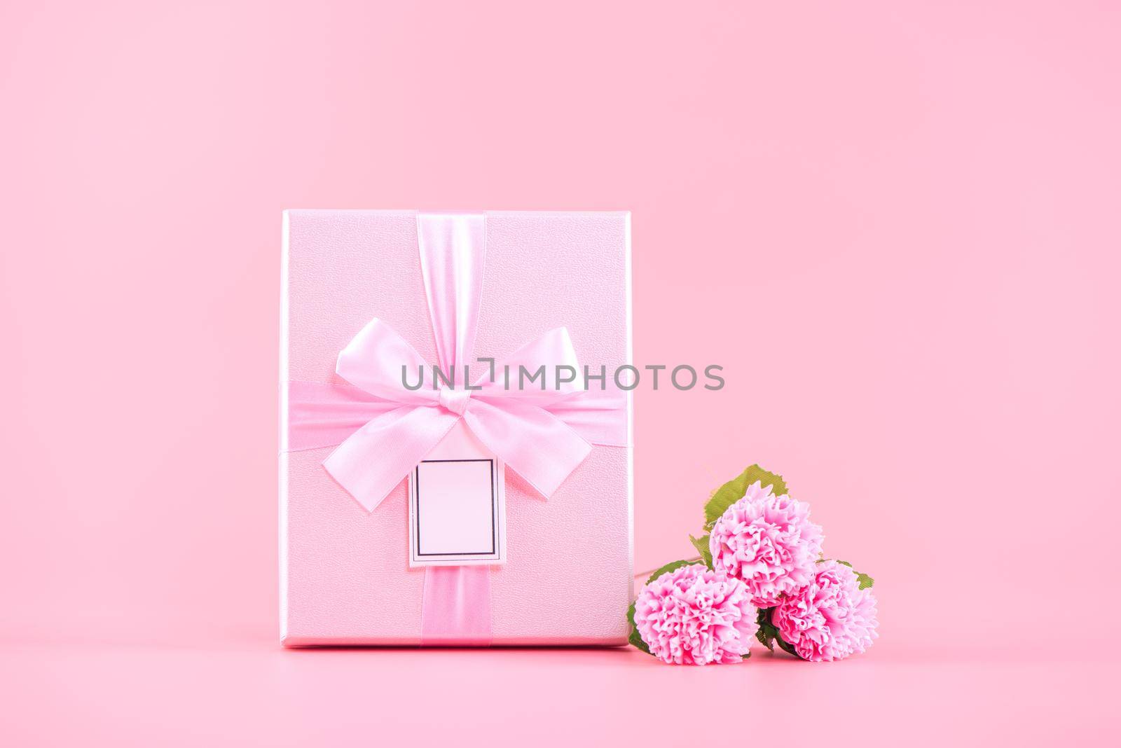 Mother's Day holiday gift design concept, pink carnation flower bouquet with wrapped gift box isolated on pink background, copy space.