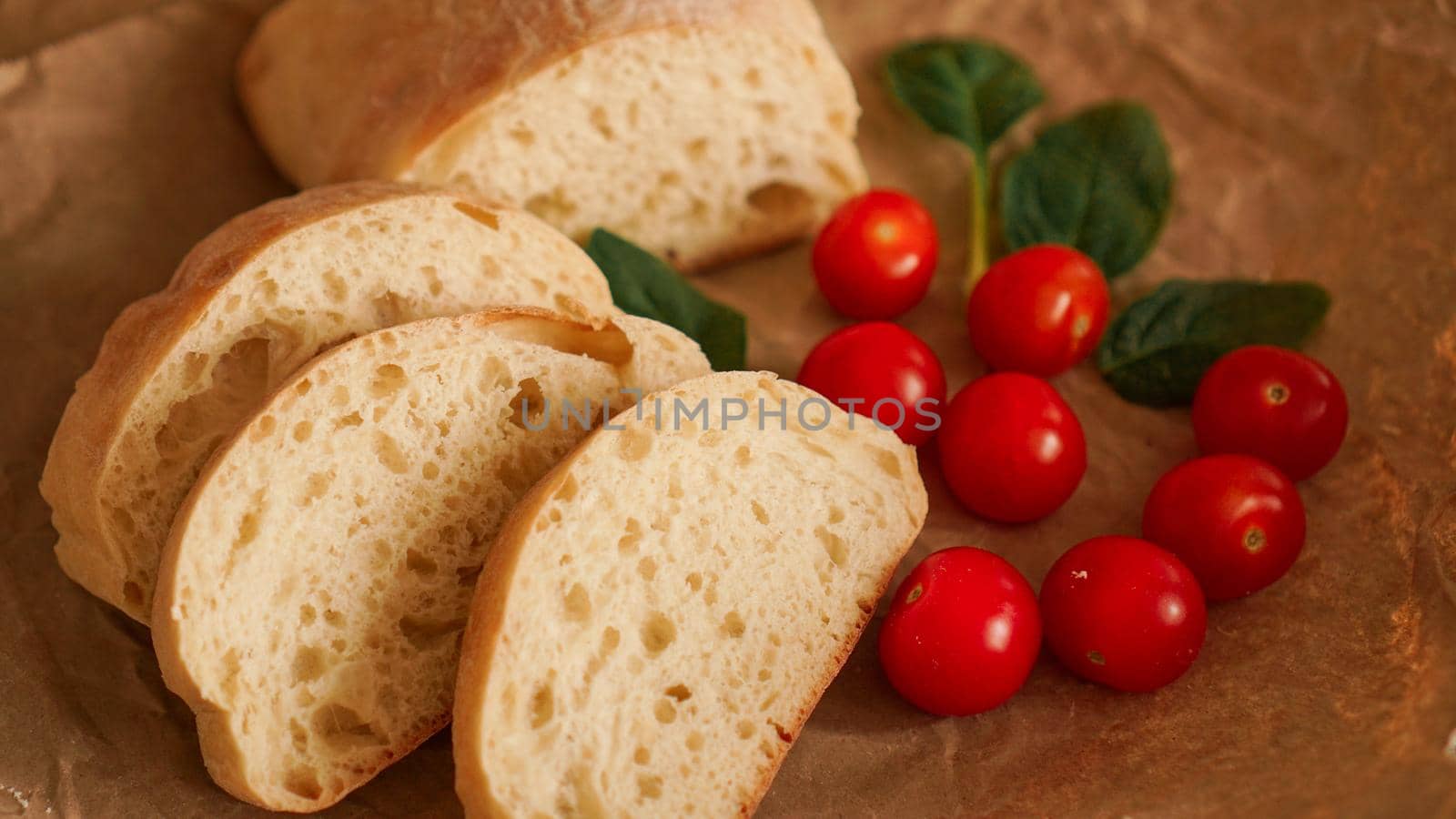 Ciabatta slices and cherry tomatoes on craft paper. by natali_brill