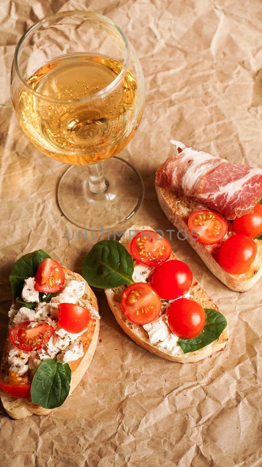 Bruschetta with cherry tomatoes. Wine glass, Italian appetizer. Craft paper background. Picnic concept
