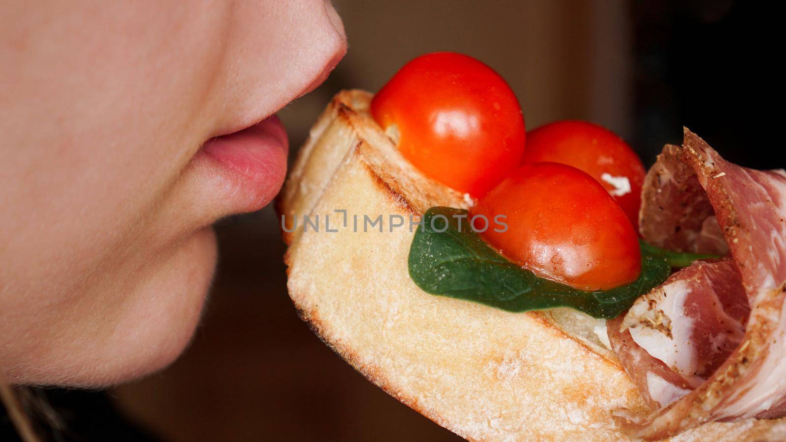 Close-up photo. Woman bites fresh bruschetta with cherry tomato by natali_brill