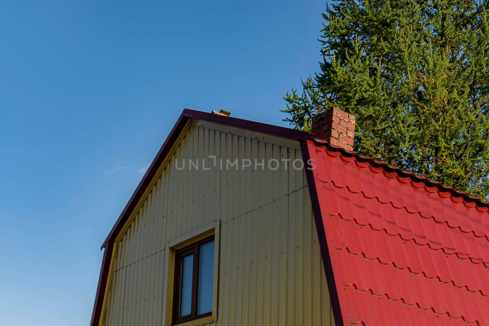 Attic red roof is made of metal from the house with a window. Outdoors of day. Back view. by Essffes