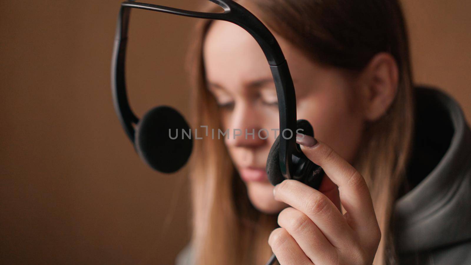 Portrait of a young girl in a hoodie puts on a headset. Call center worker. Remote work from home. Brown tones pictures