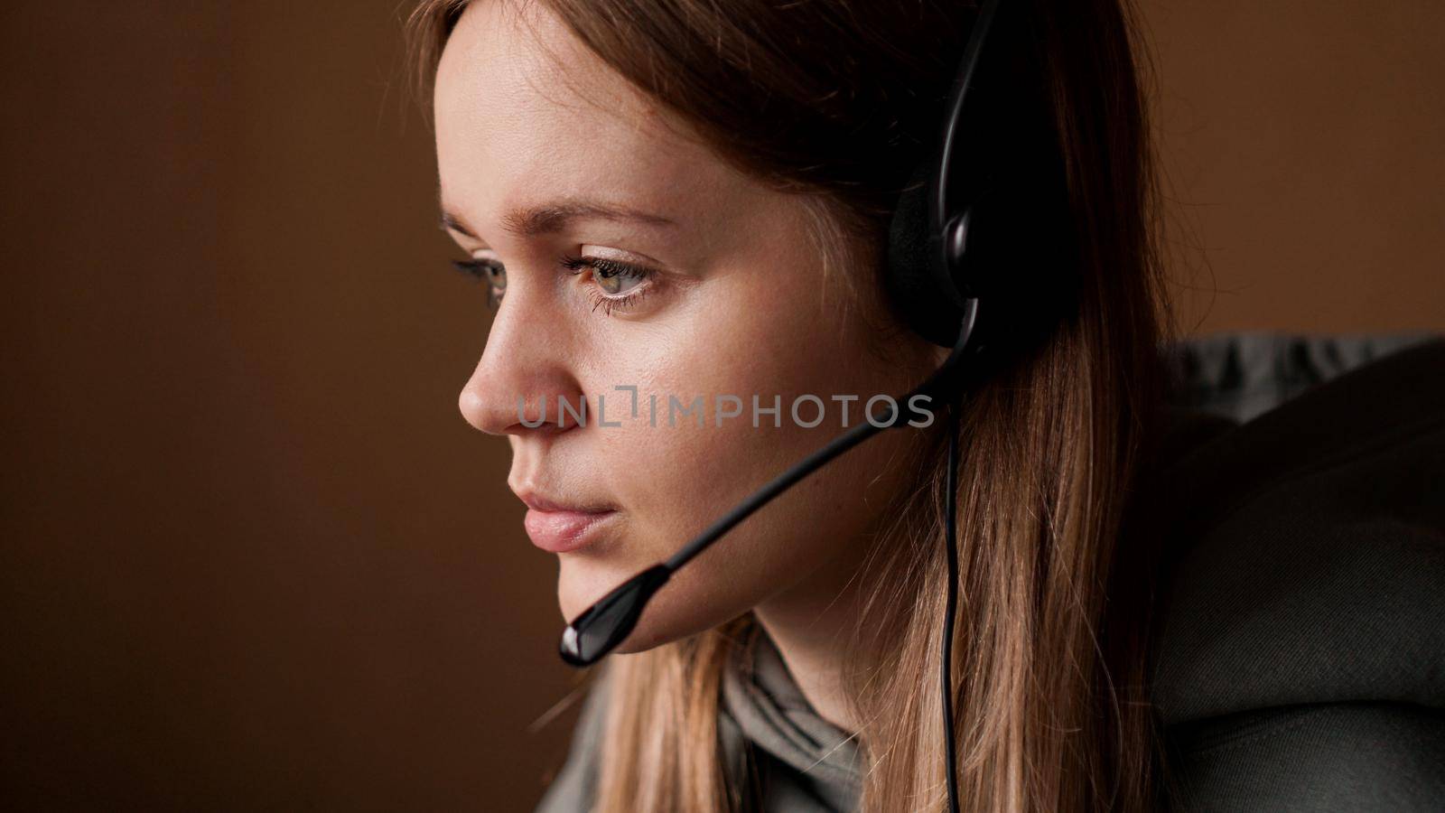Portrait of a young girl in a hoodie and with a black headset. Call center worker. Remote work from home. Brown tones pictures