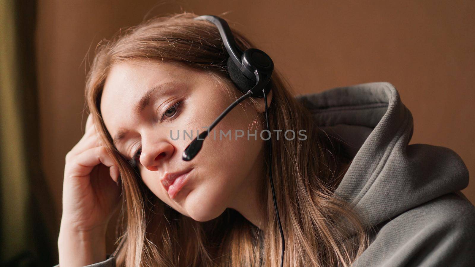 Portrait of a young girl in a hoodie and with a headset. Tired girl streamer or call center worker.