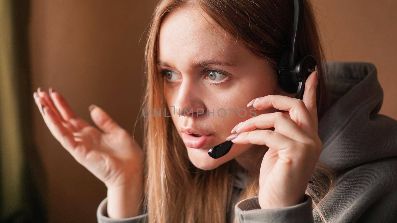 Confused girl operator with headset. Remote work from home in a call center. Emotional girl. Hands to the side. Irritable conversation with a client