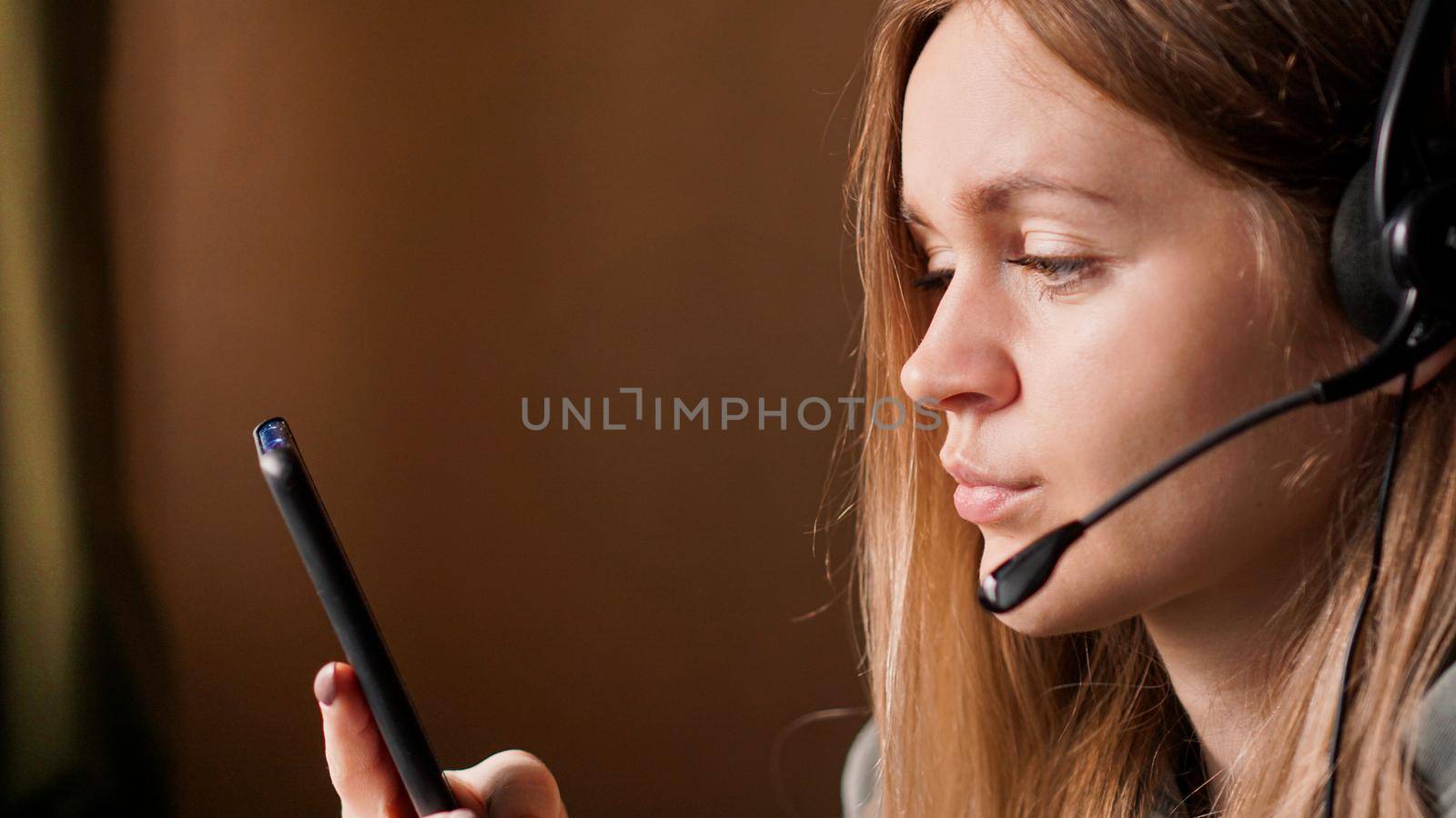 Portrait of a young girl in a hoodie and with a headset. Call center worker. Remote work from home. Brown tones pictures