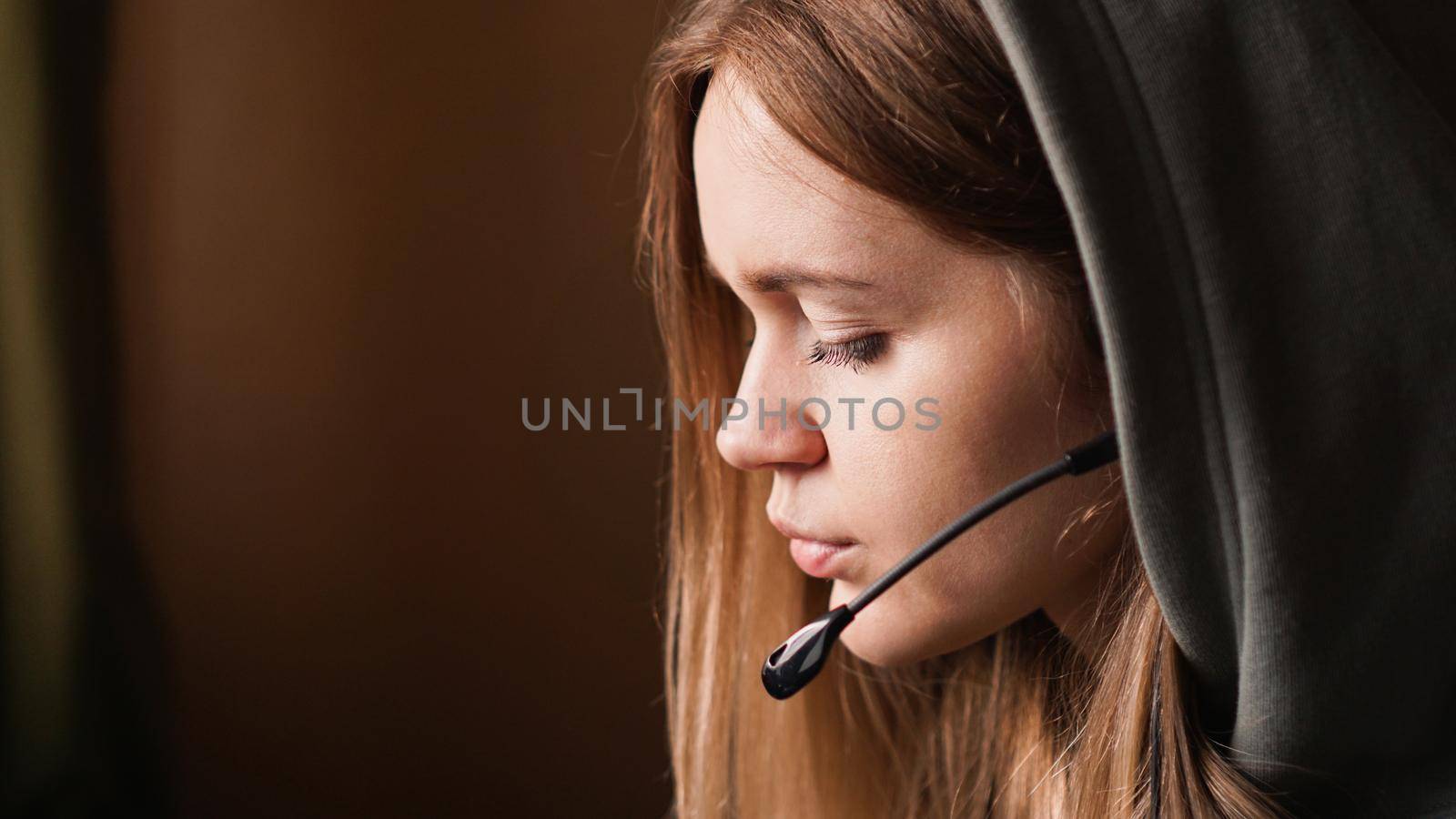 Portrait of a young girl in a hoodie and with a headset. Call center worker. Beautiful girl in the hood. Remote work from home. Brown tones pictures