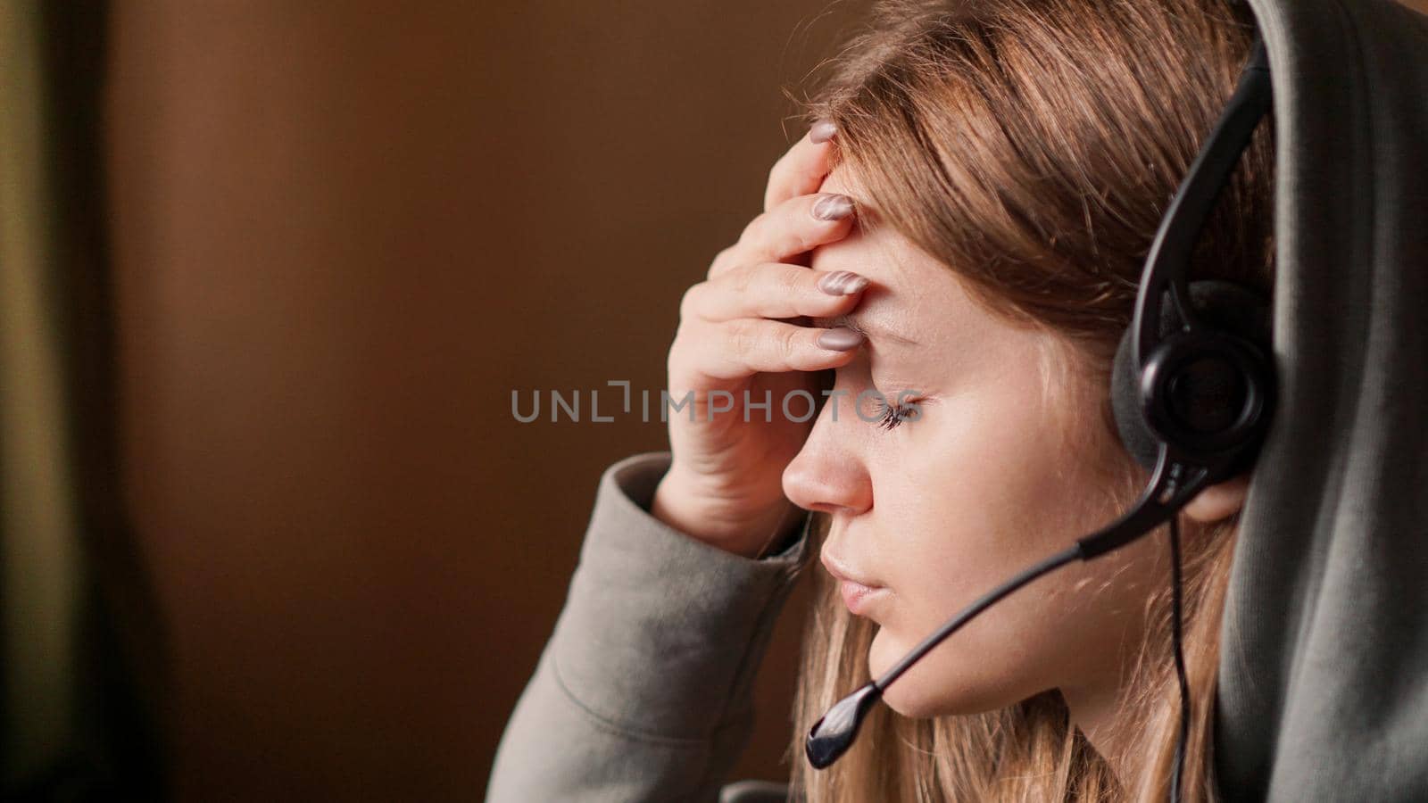 Portrait of young girl in a hoodie and with a headset. Tired call center worker by natali_brill