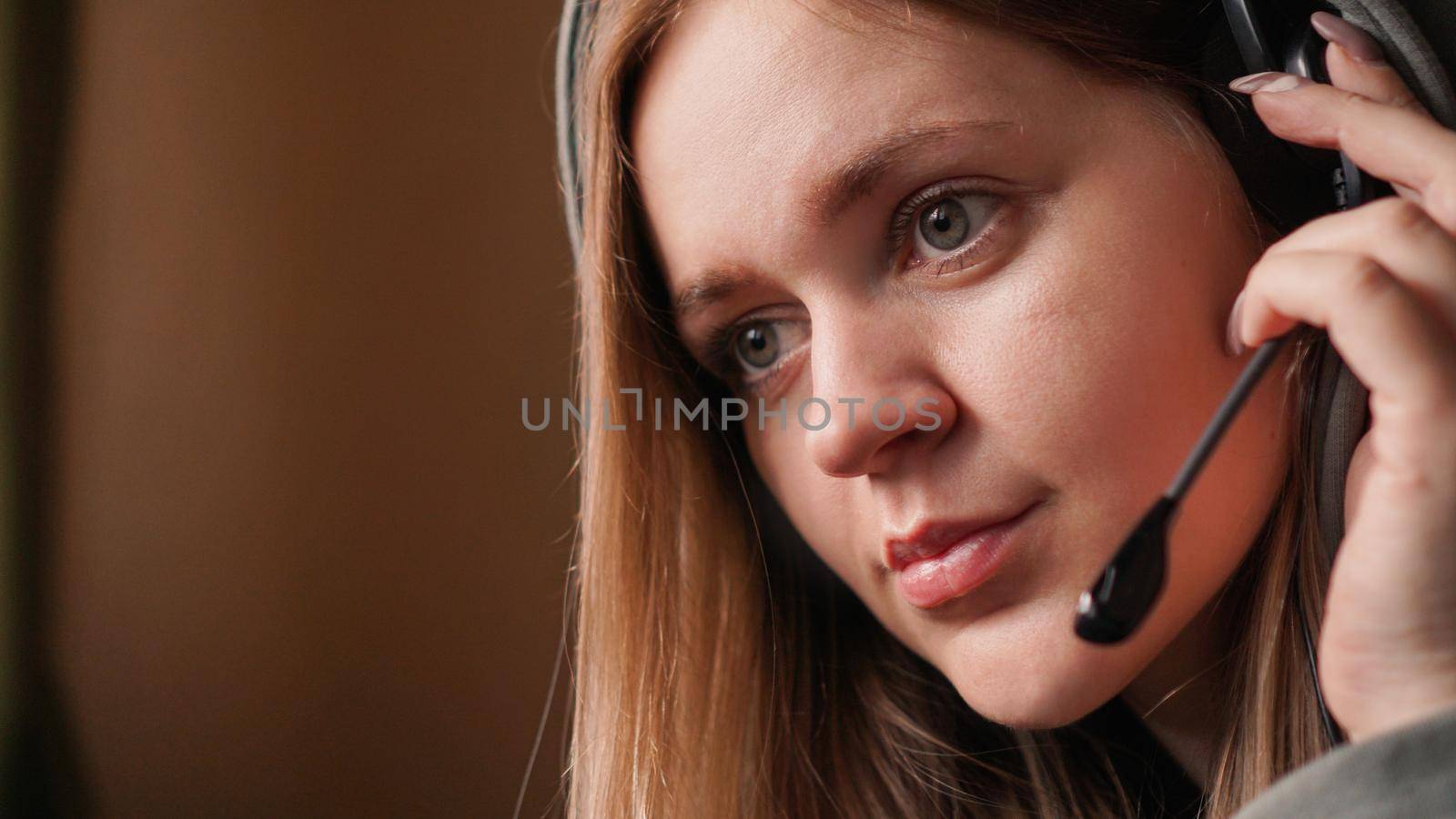 Portrait of a young girl in a hoodie and with a headset. Call center worker. Remote work from home. Brown tones pictures