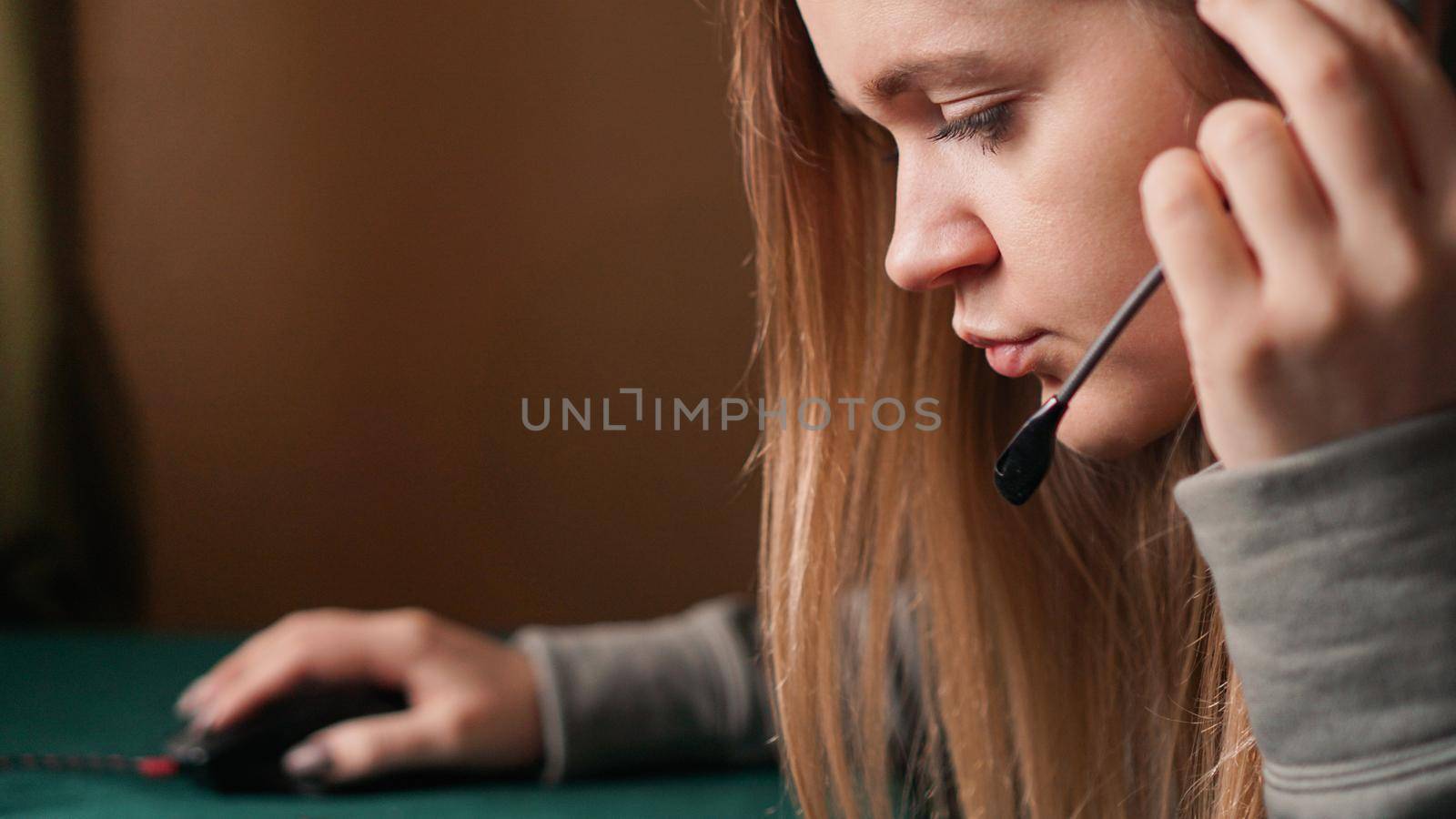 Portrait of a young girl in a hoodie and with a headset. Call center worker. She holds the earpiece to hear the client better. Communication problems. Remote work from home. Brown tones pictures