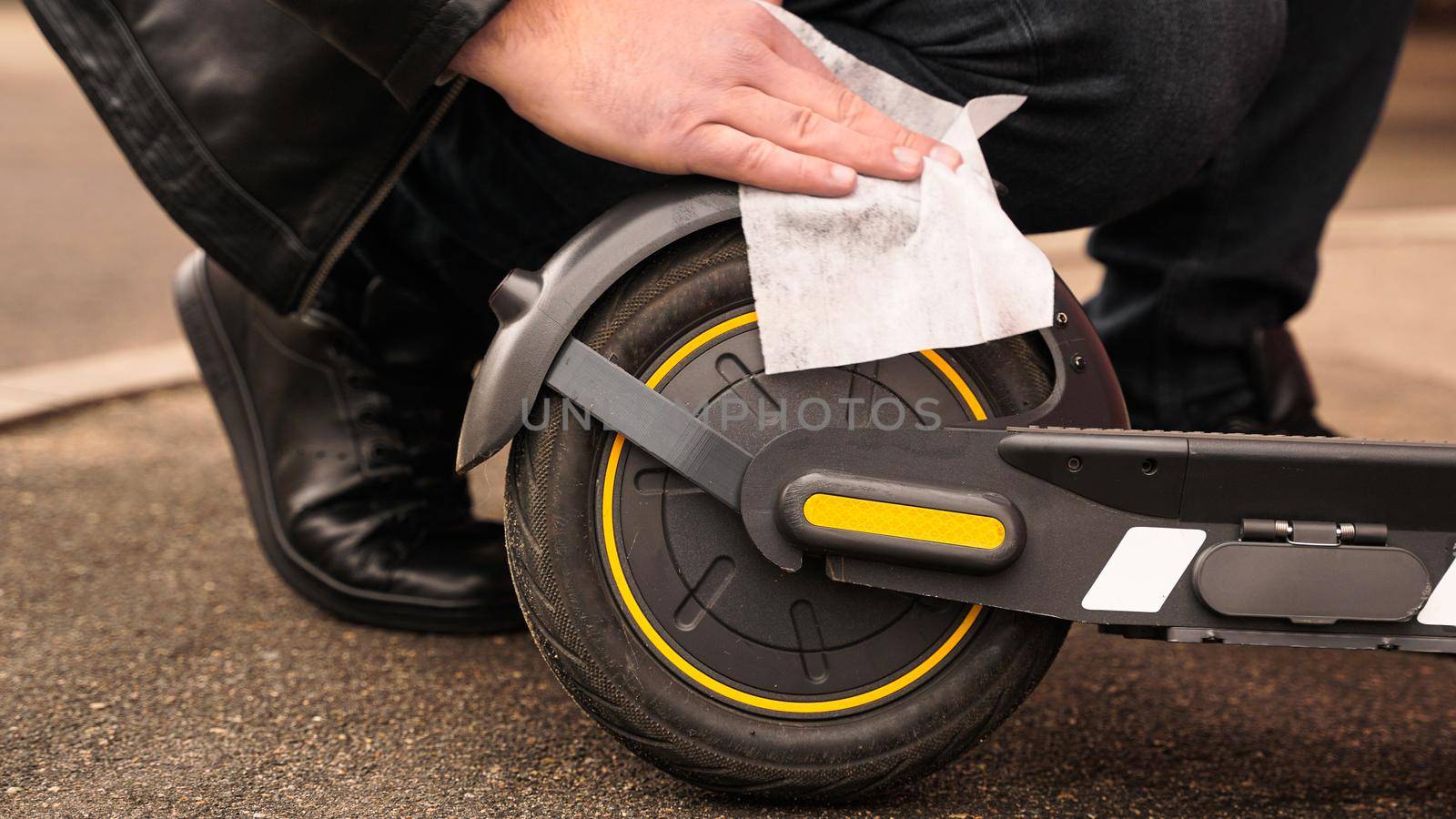 A man wipes his electric scooter with a white damp cloth. Cleaning dirty scooter. Close-up photo
