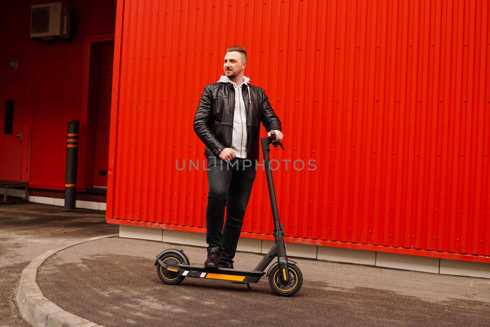 Young attractive man on electric scooter over red background by natali_brill