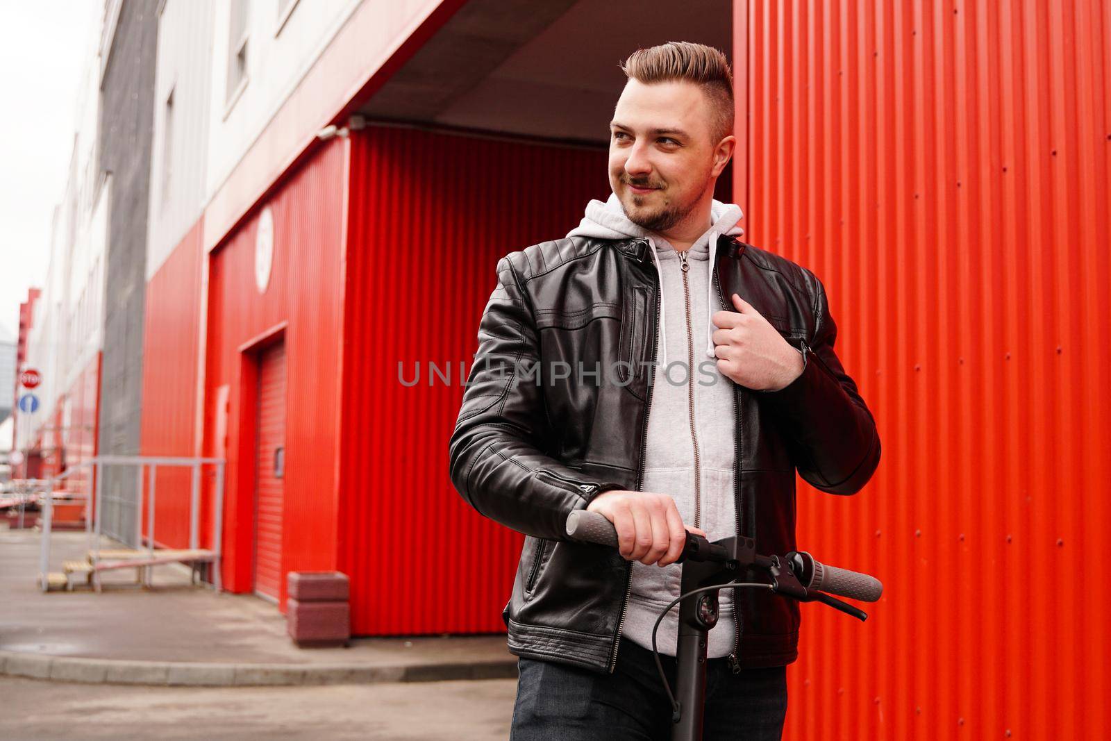 Young attractive man on electric scooter over red background. Urban transport