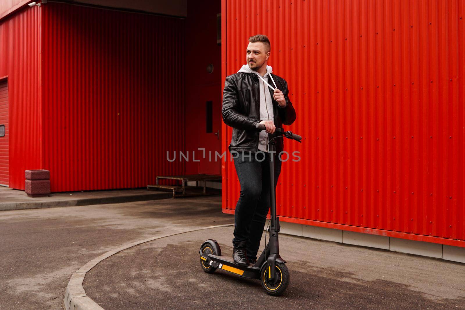 Young attractive man on electric scooter over red background. Urban transport