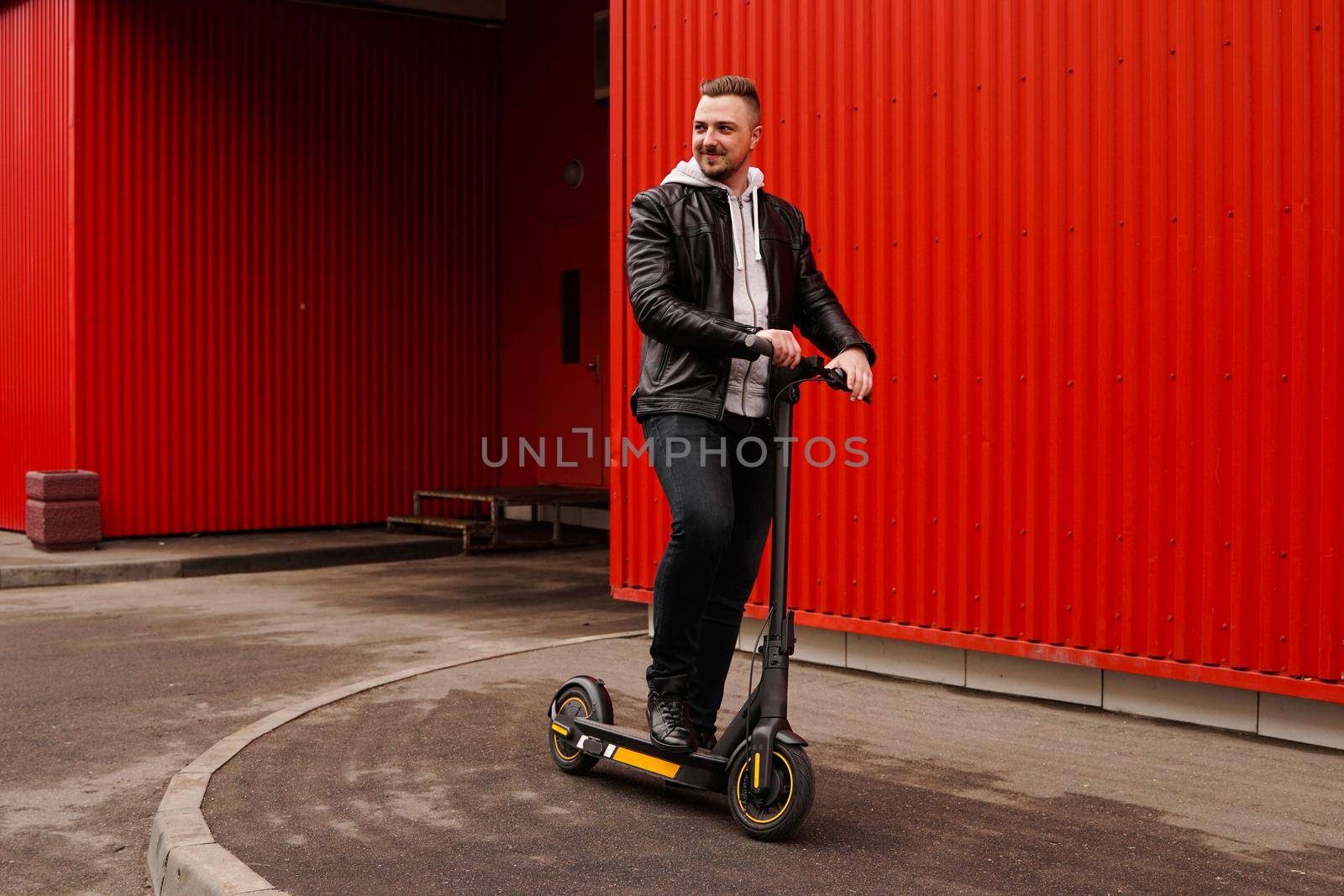 Young attractive man on electric scooter over red background. Urban transport